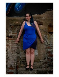 woman with blue hair leaning on a brick wall