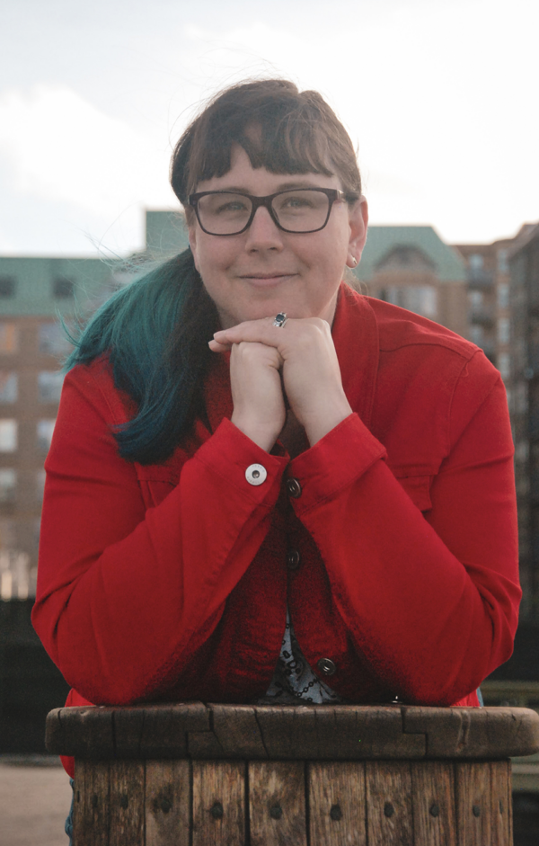A photo of Amy wearing a red jacket, glasses and resting her chin on her fists
